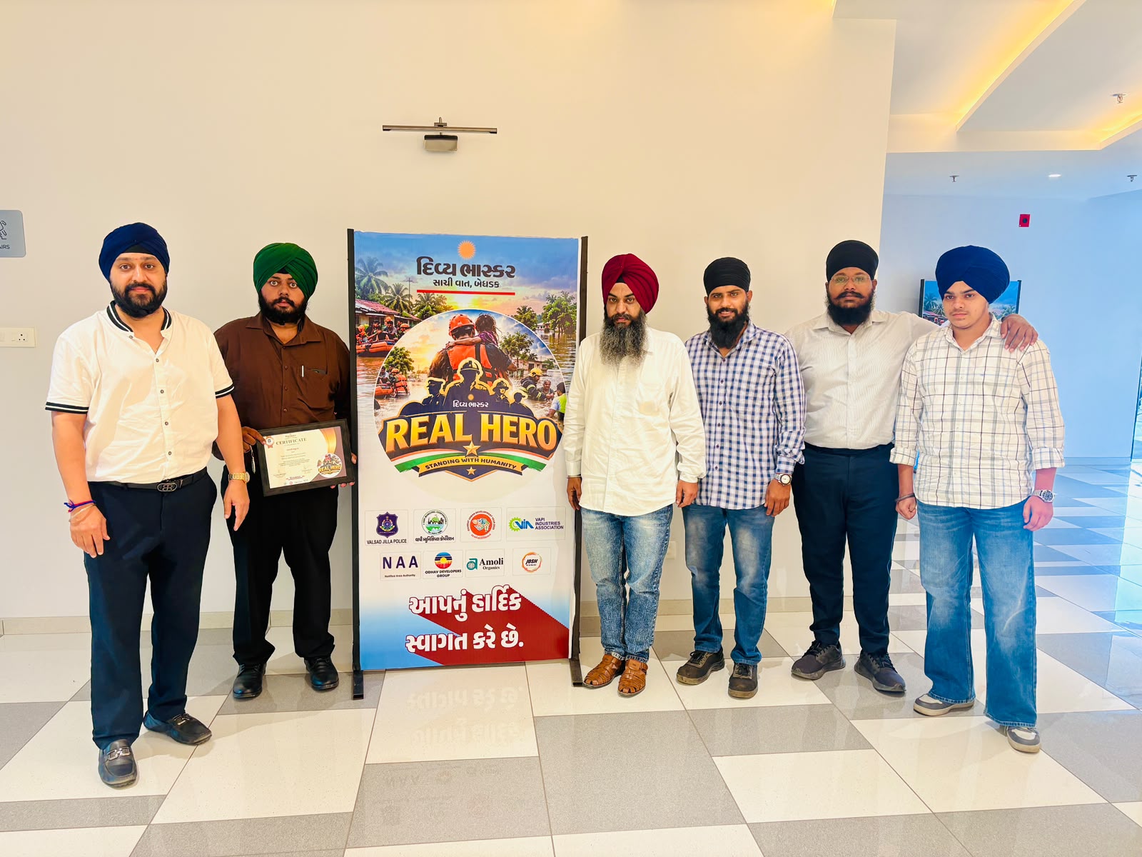 VPCF Punjabi Samaj members standing beside the REAL HERO flood-relief recognition banner